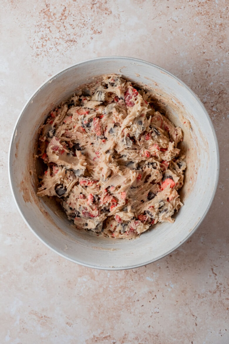 Cookie dough in mixing bowl with chunks of chocolate and strawberries.